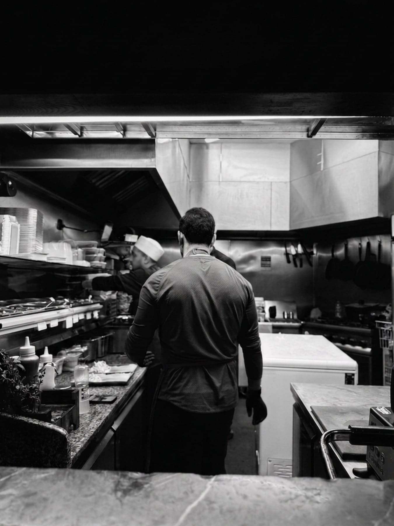 A chef at the pass in a working kitchen, the line stretching away behind